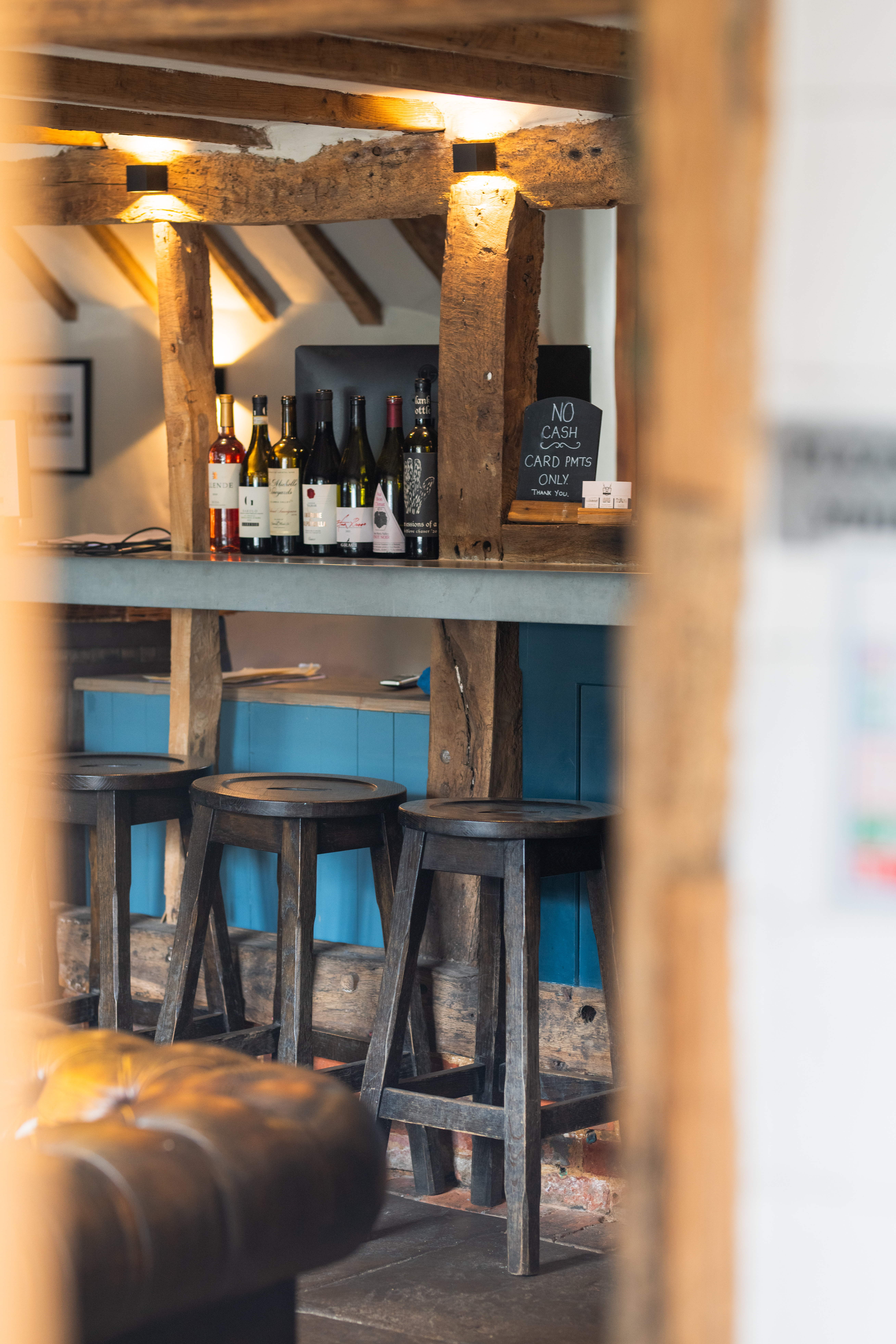 Bar with bar stools in front, a chesterfield couch in view and wooden beams.