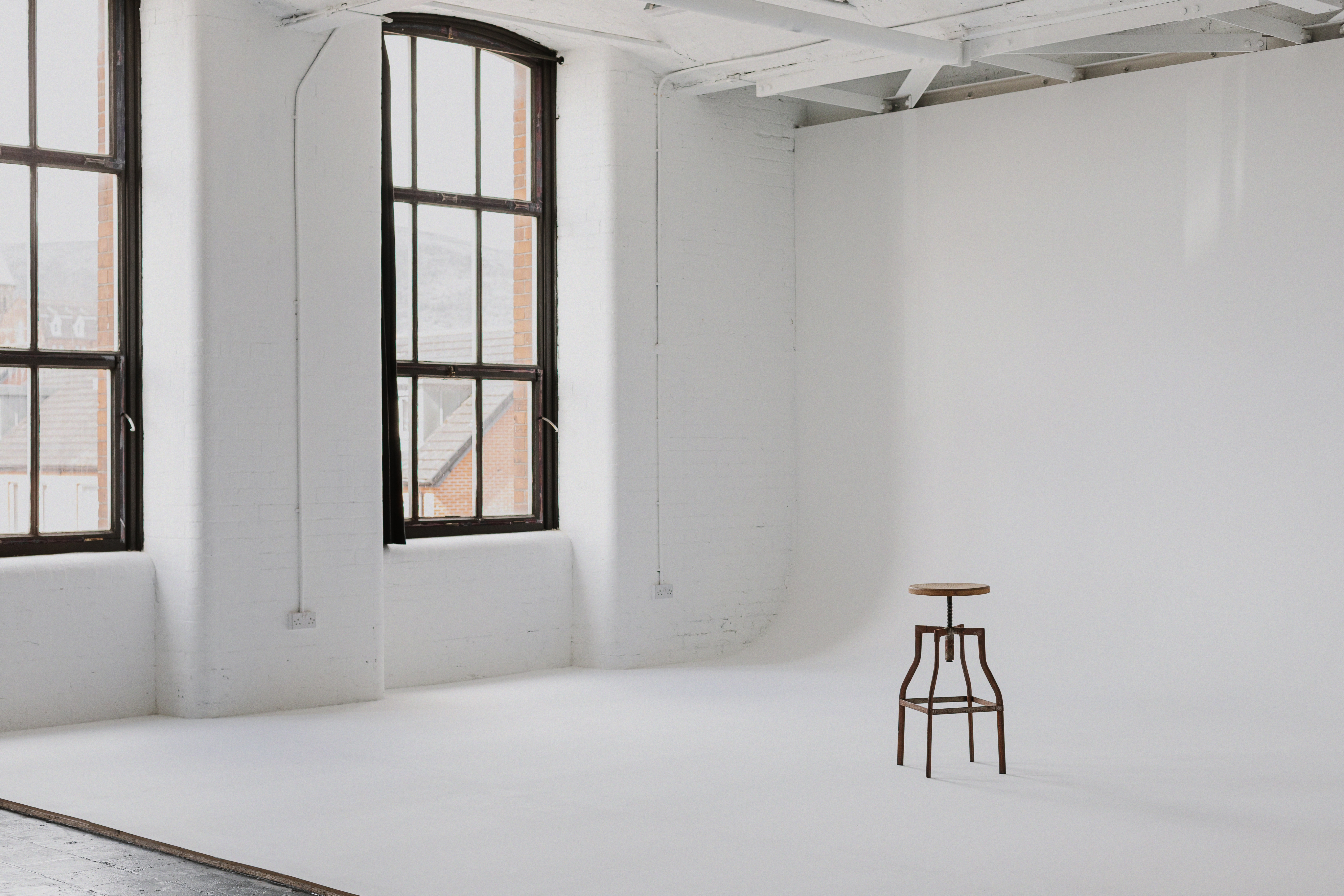 White cyclorama studio beside large industrial windows with a single stool.