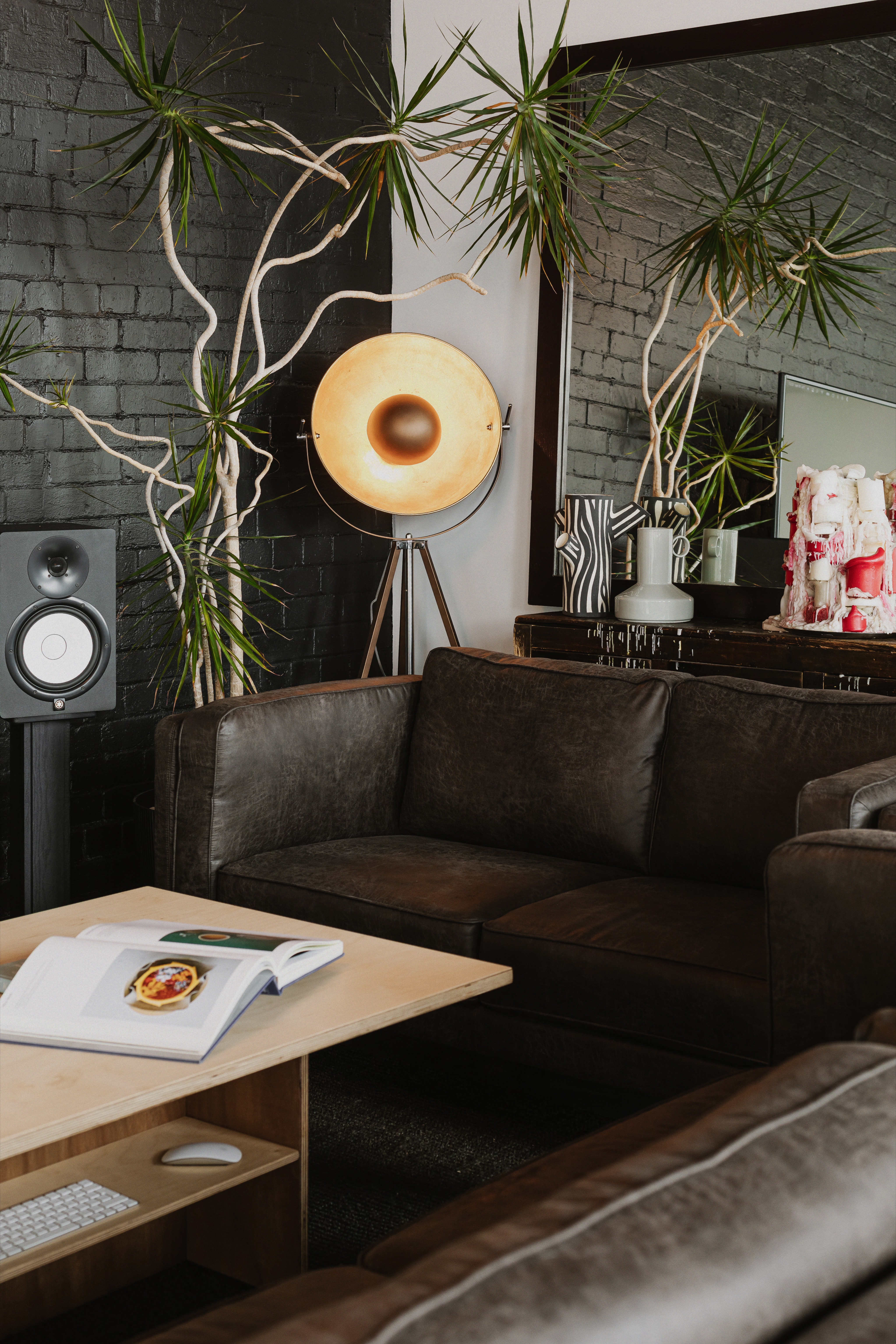 Leather sofa, indoor plants and vintage floor lamp against black brick wall.