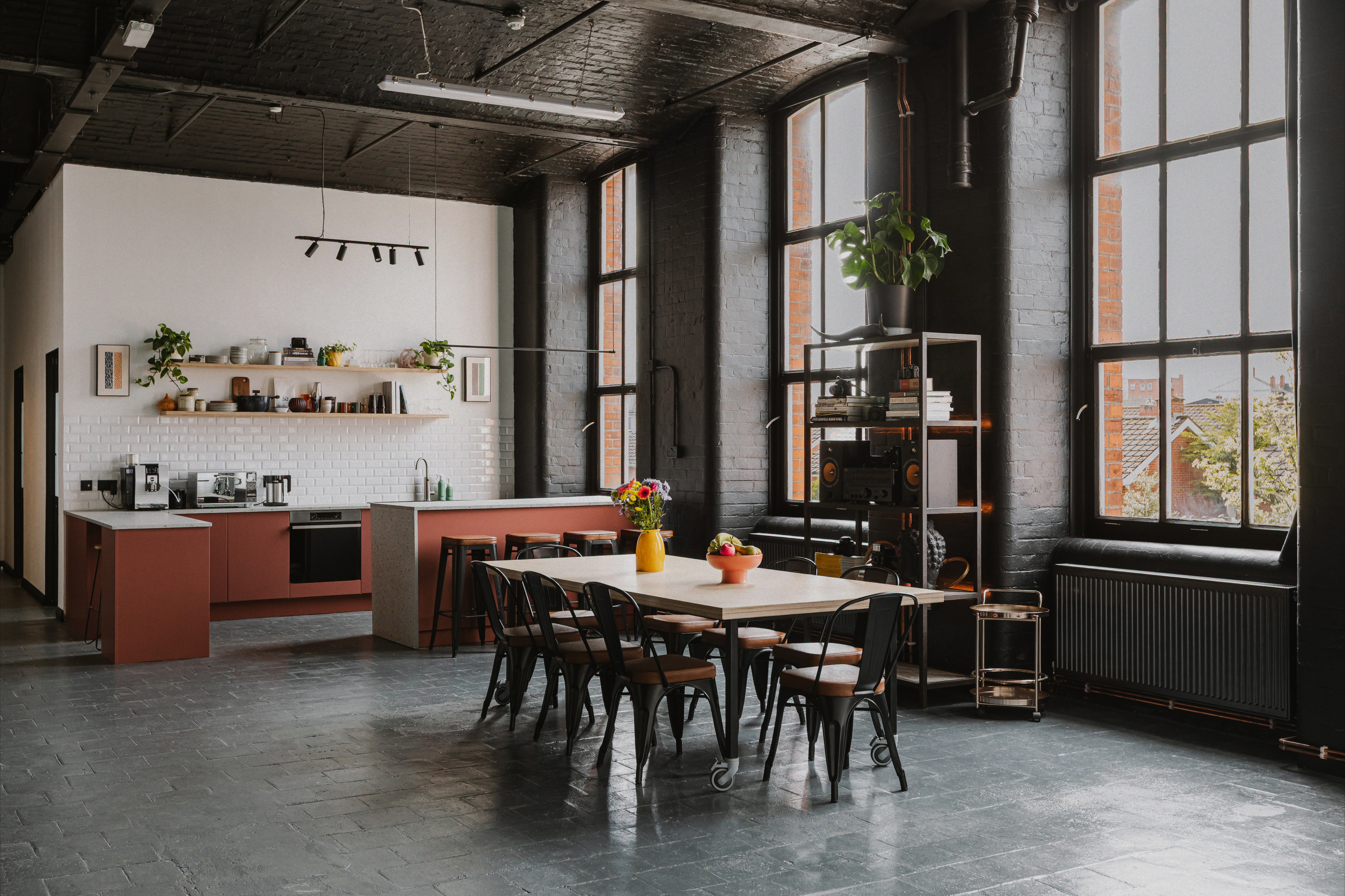 Open-plan kitchen and dining set with tall windows and black brick walls.