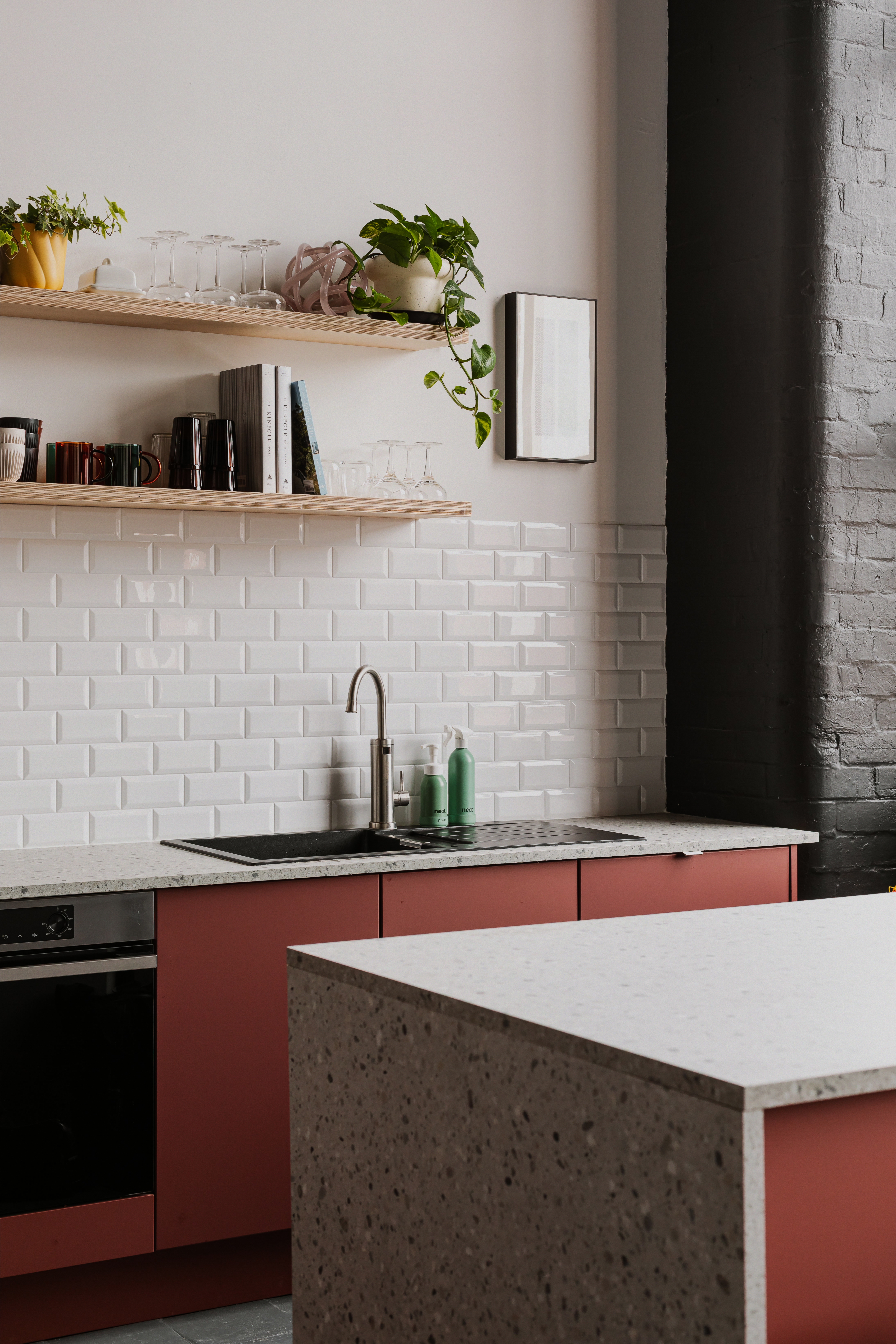 Modern studio kitchen with red cabinetry, stone worktops and open shelving.