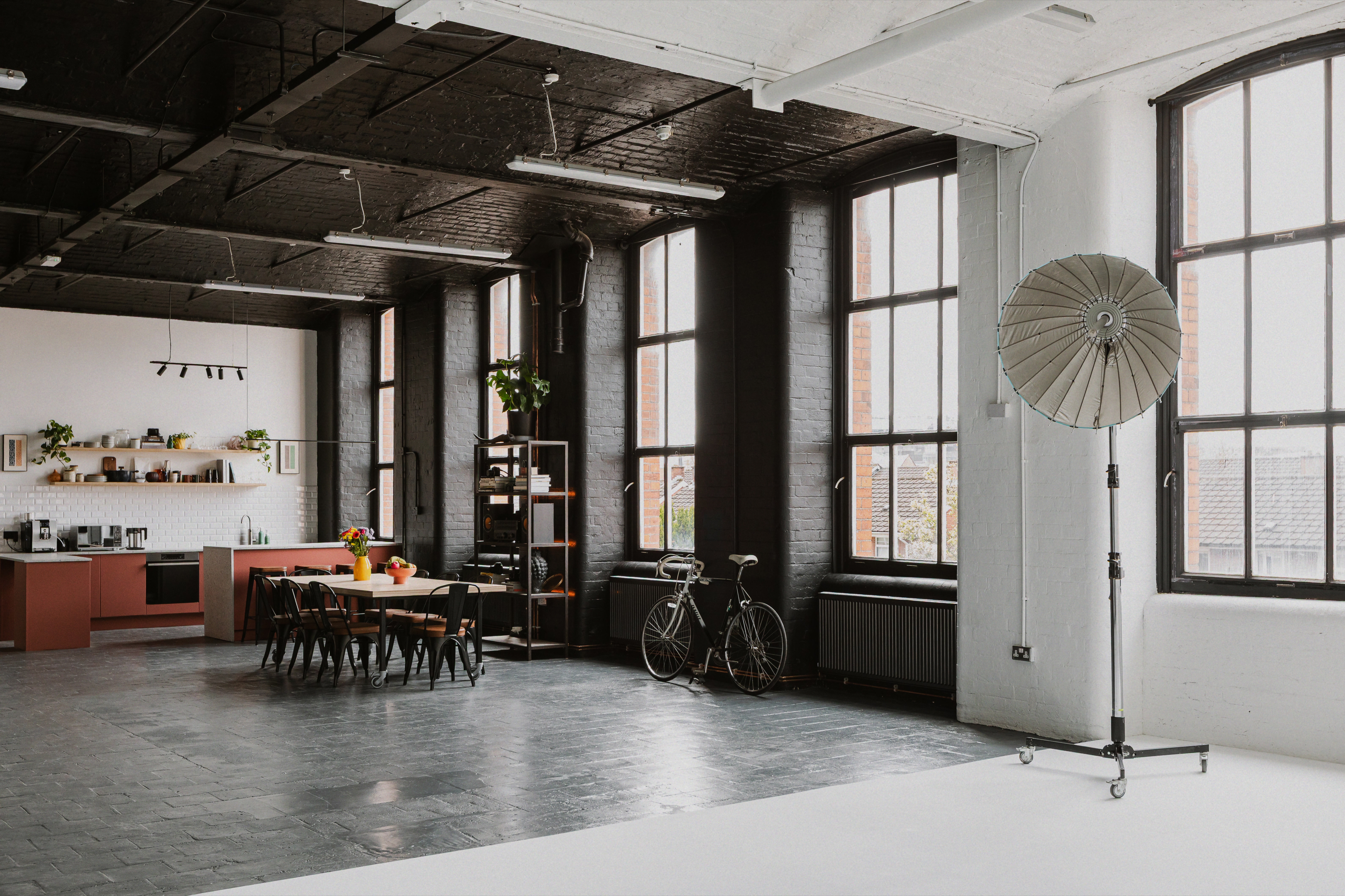 Large industrial studio interior with kitchen, tall windows and open shooting space.