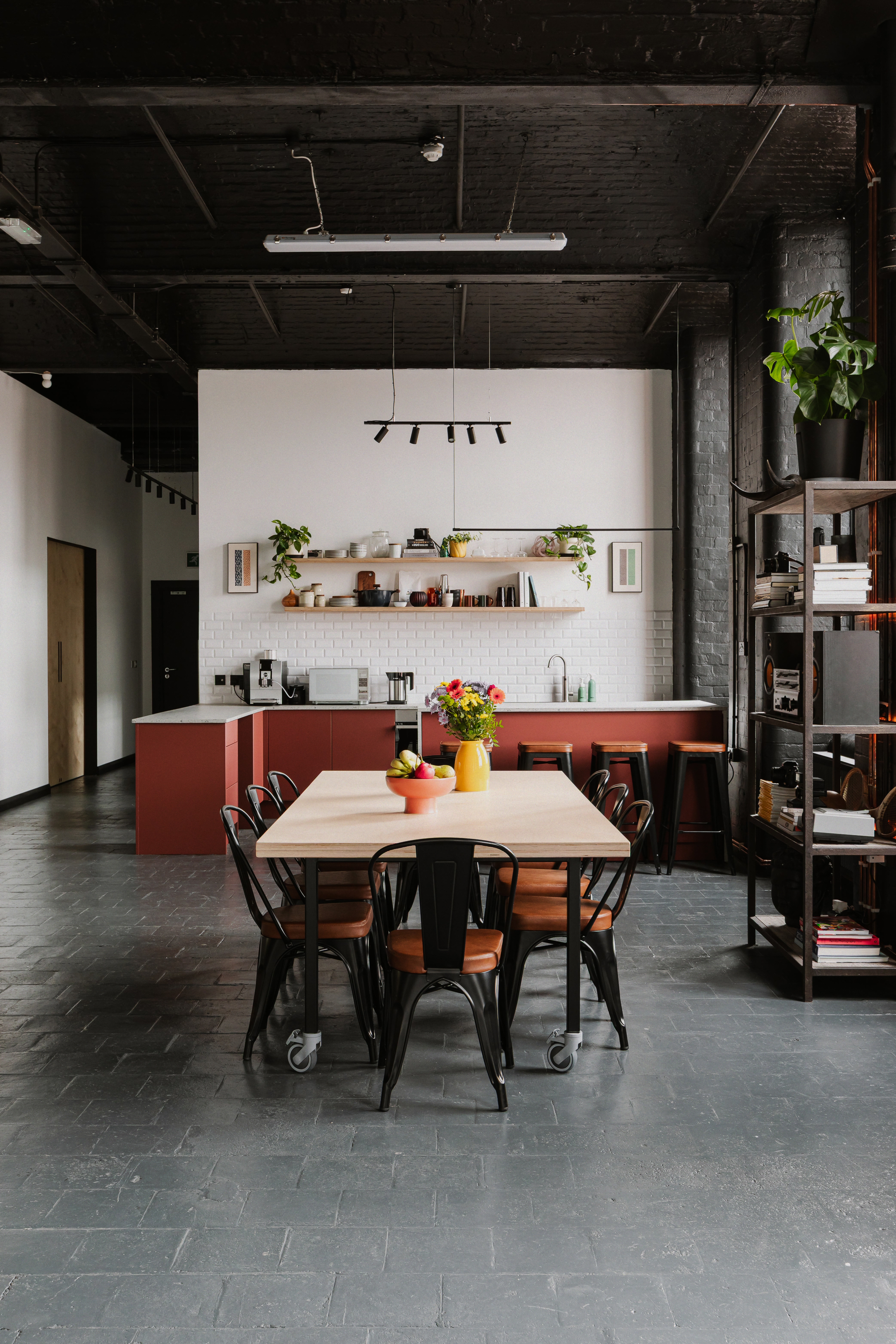 Dining table and red kitchen beneath a black industrial ceiling in Belfast studio.