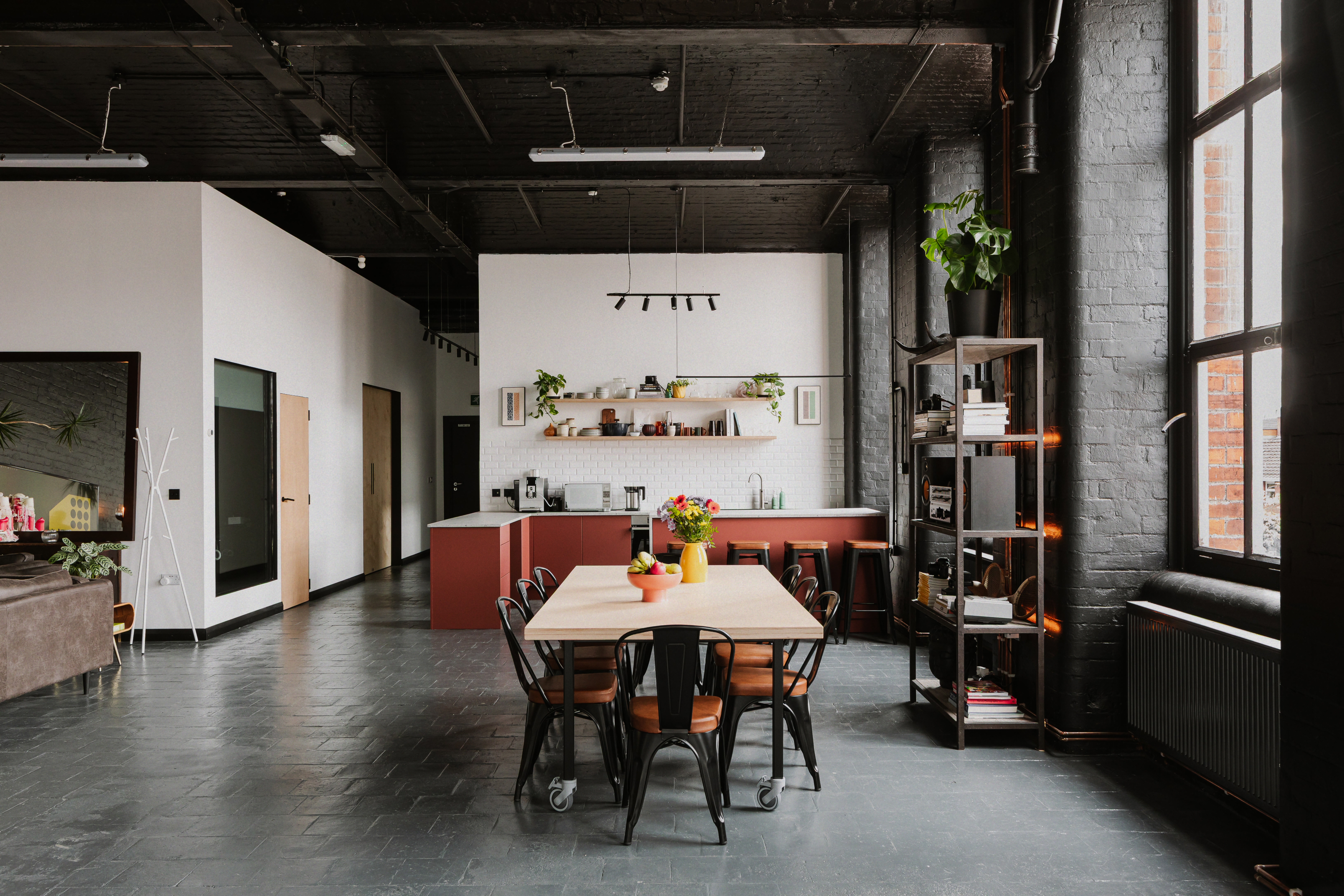 Industrial kitchen and dining area beside large natural-light studio windows.