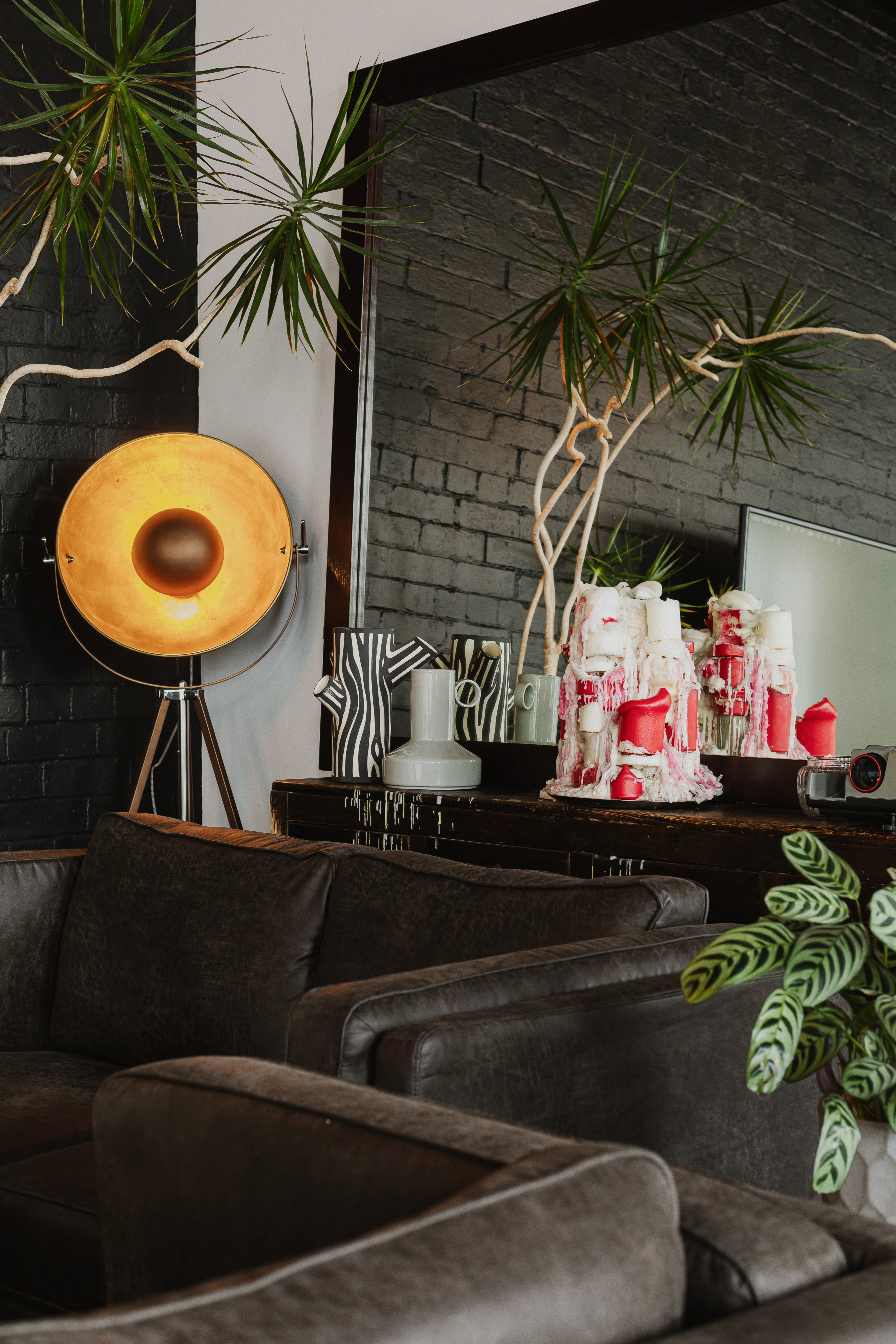 Leather lounge with large mirror, plants and warm vintage lamp against black brick.